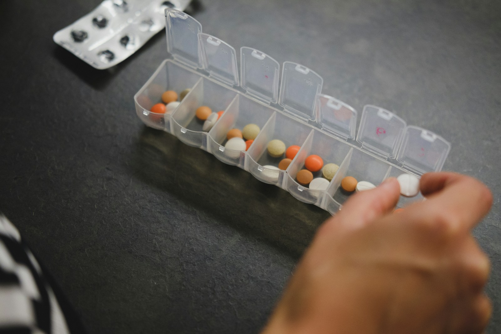 A hand taking a pill from a weekly pill organizer
